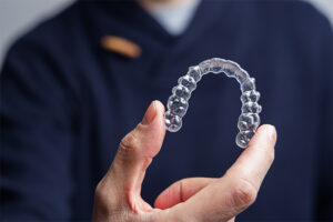 A person holds a clear plastic tooth in their hand, showcasing its transparent design and dental features.