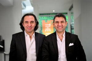 Two men in suits standing side by side, both smiling and looking towards the camera.